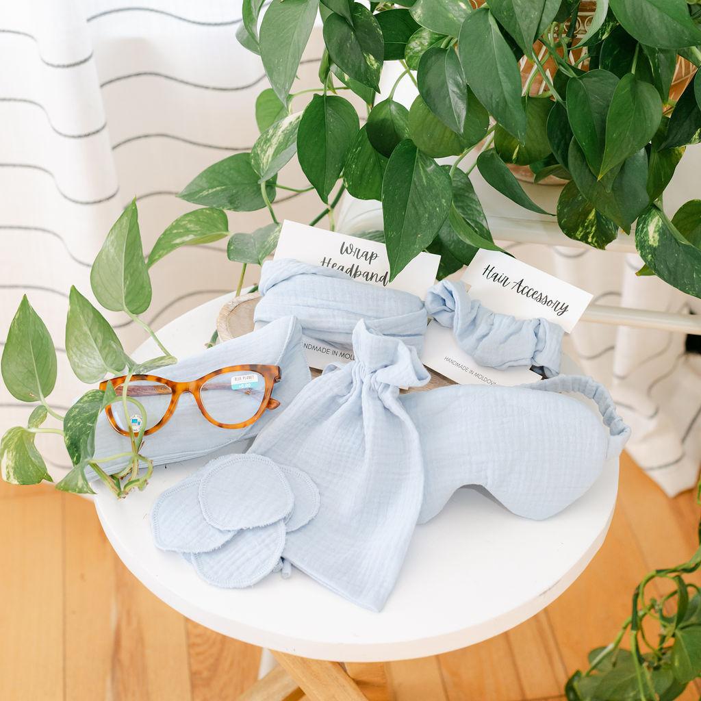 A collection of light blue muslin accessories on a white table with a plant in the background.