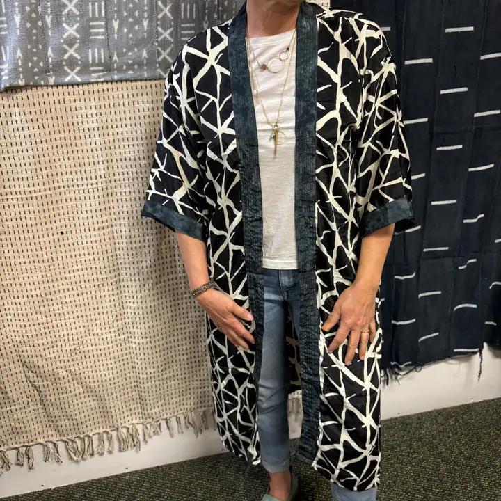 Person wearing a black and white patterned kimono standing in front of textured walls.
