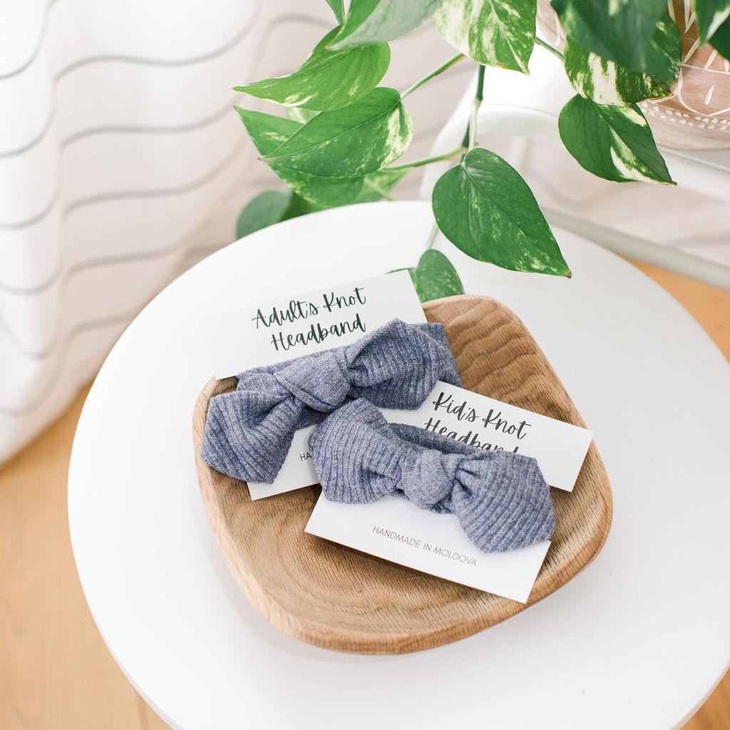 Two blue knot headbands in a wooden bowl on a white table with a plant in the background