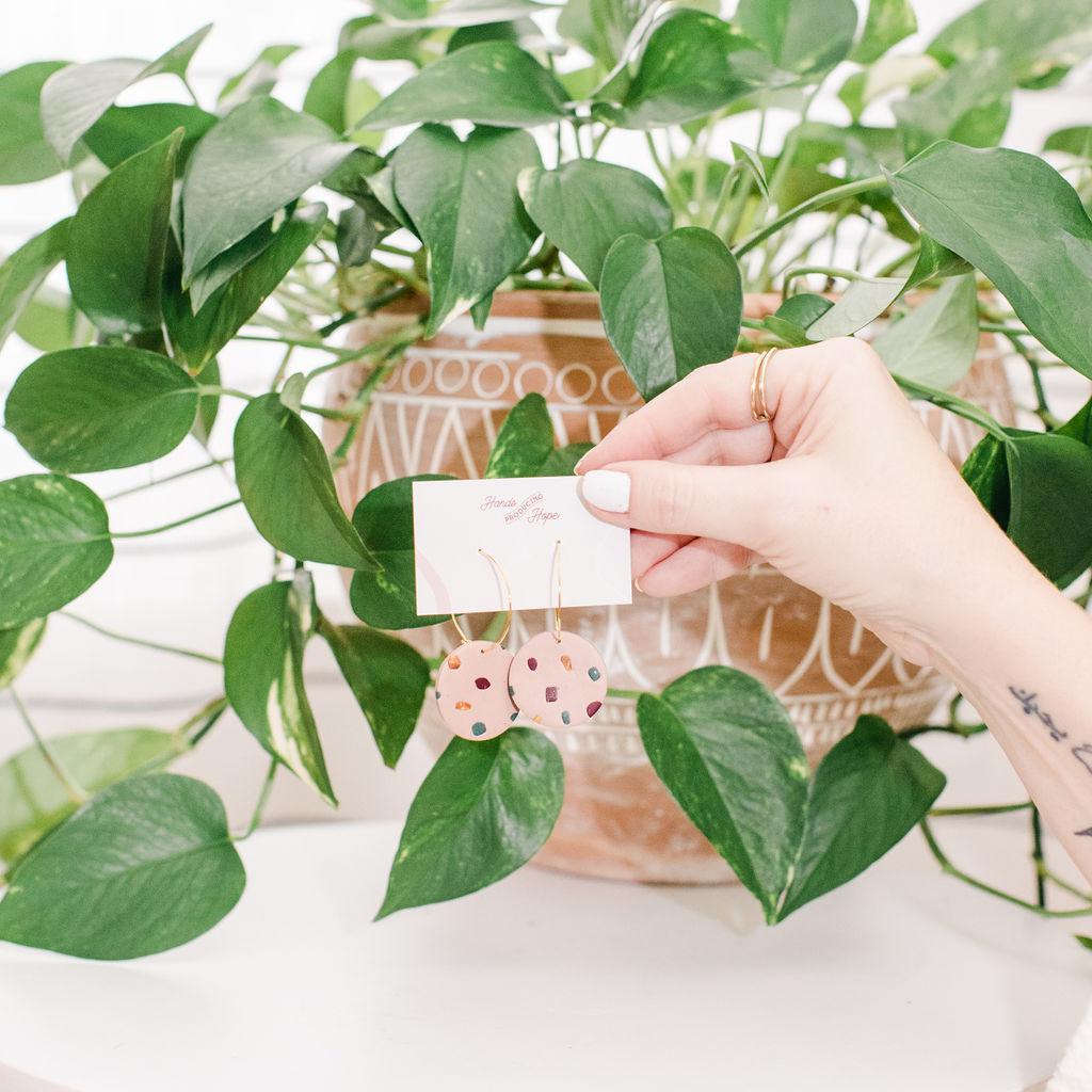 Hand holding a card with earrings in front of a green plant