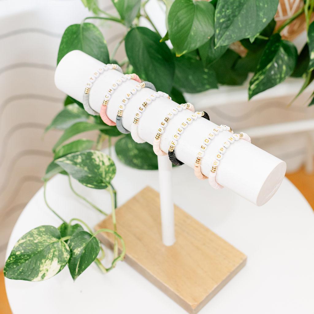 A display holding multiple bracelets on a white surface with a plant in the background