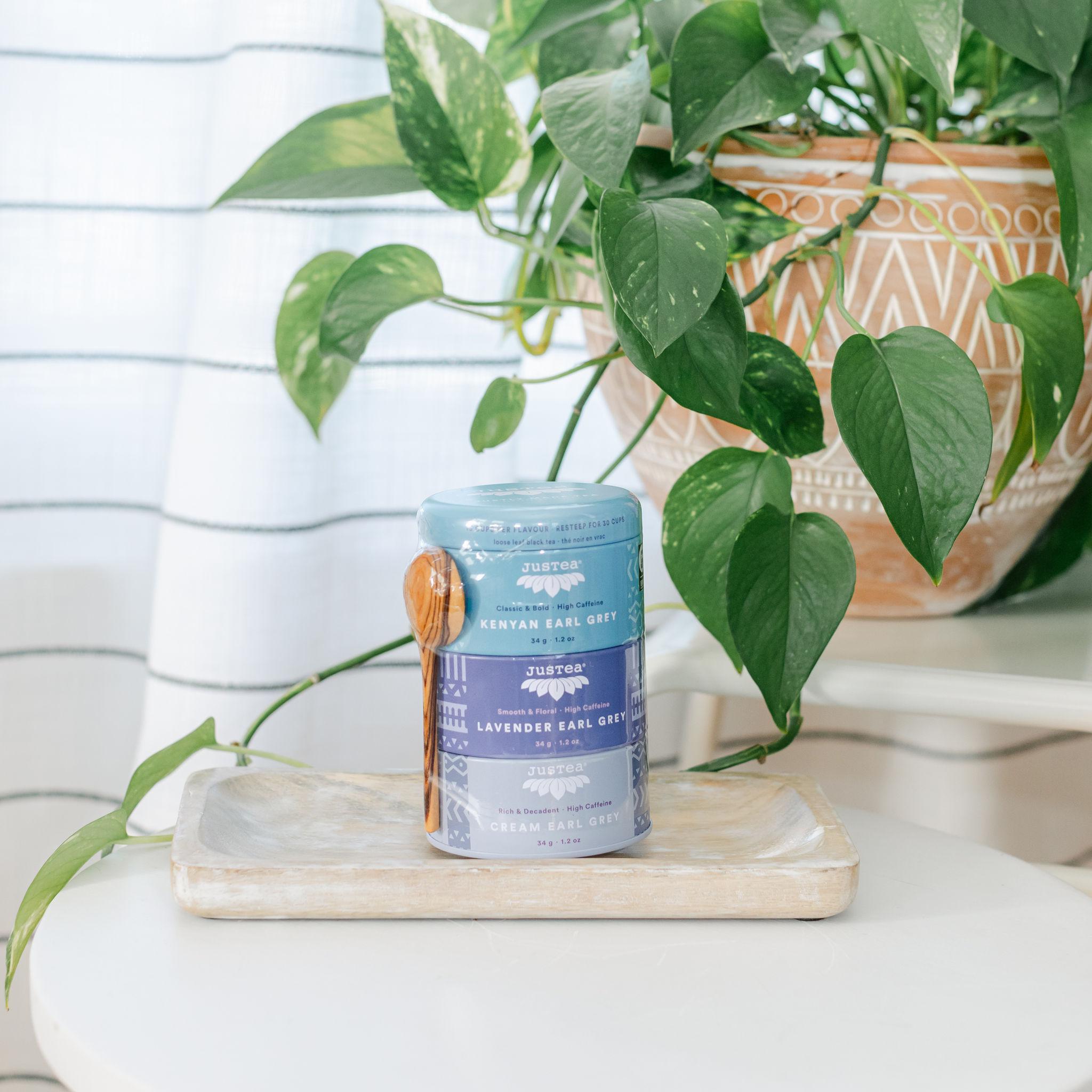 A tin container of Earl Grey tea leaves with a label showing different flavors, placed on a wooden surface with a plant in the background.