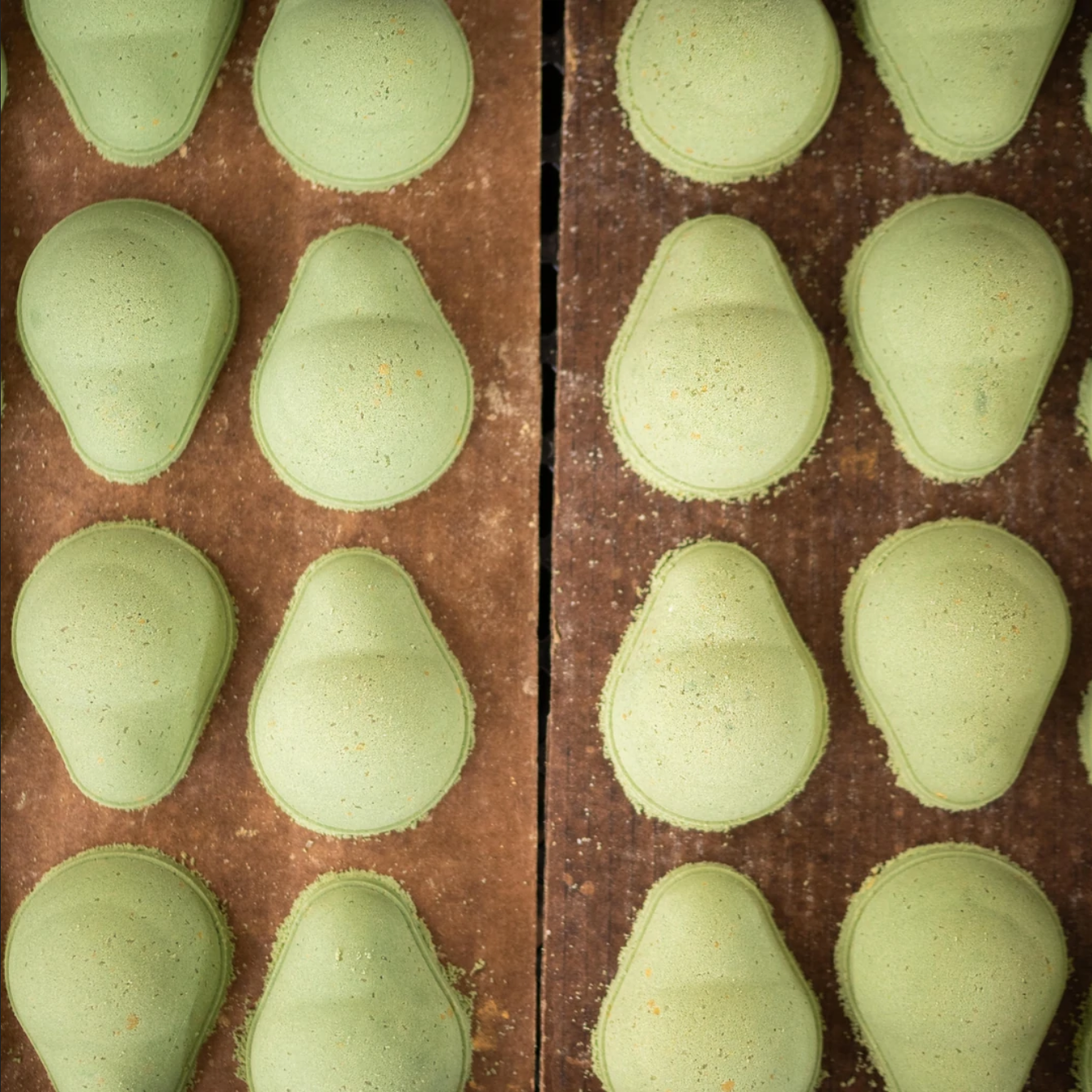 Green bath bombs shaped like avocados on a wooden table.