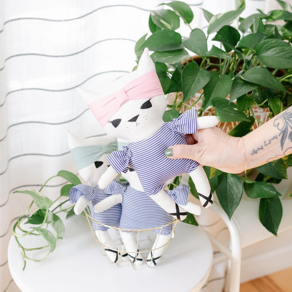 A person holding a stuffed cat toy with blue stripes and a headband with a plant in the background