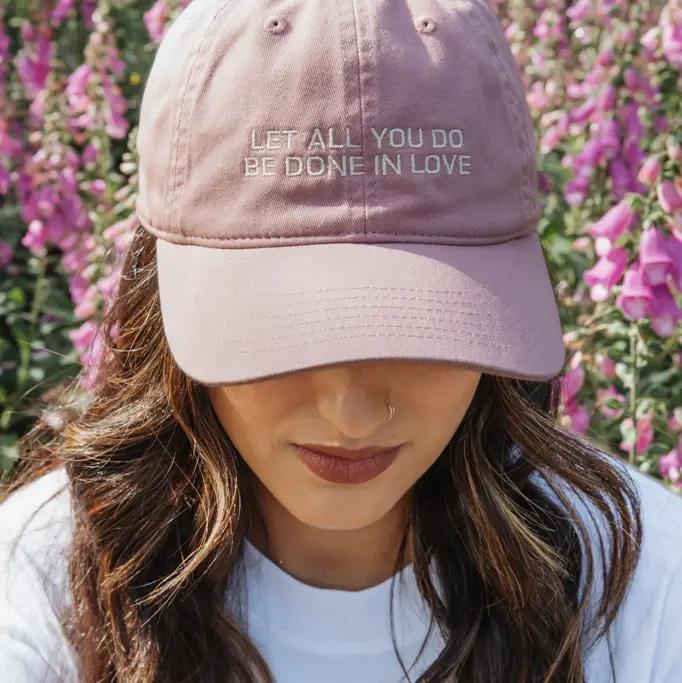 Person wearing a pink cap with text in front of pink flowers