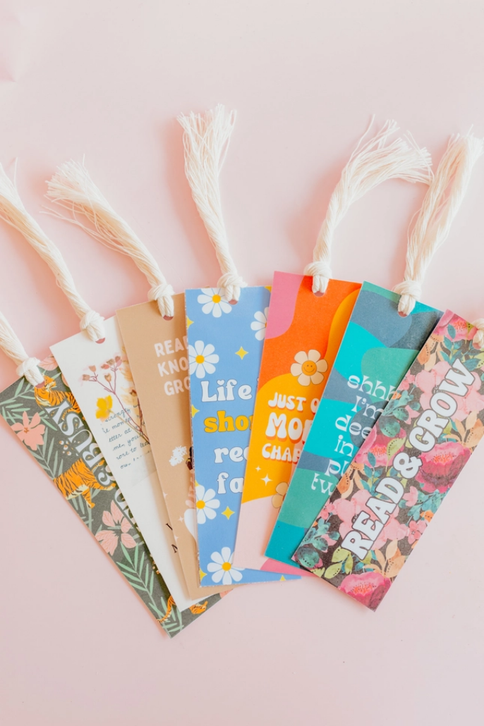 Multiple colorful bookmarks with phrases on them laying on a light pink background