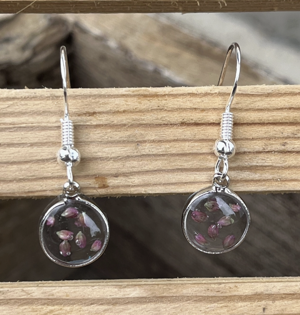 A pair of silver earrings with acrylic flower pedals hanging on a piece of wood