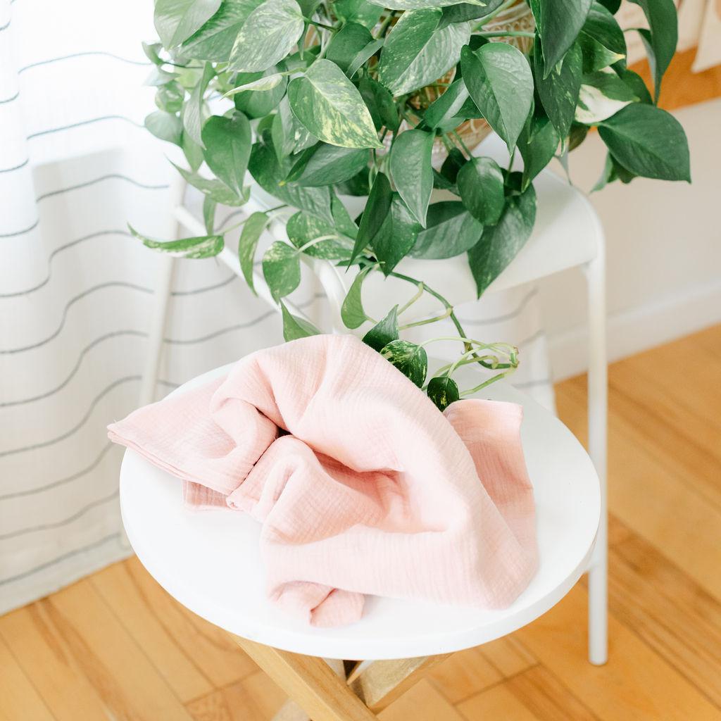 A pink muslin baby wrap on a white table with a plant in the background