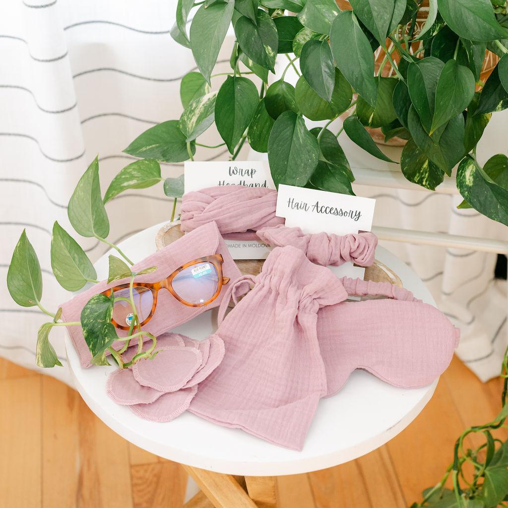 Pink muslin products displayed on a wooden tray with a plant in the background.