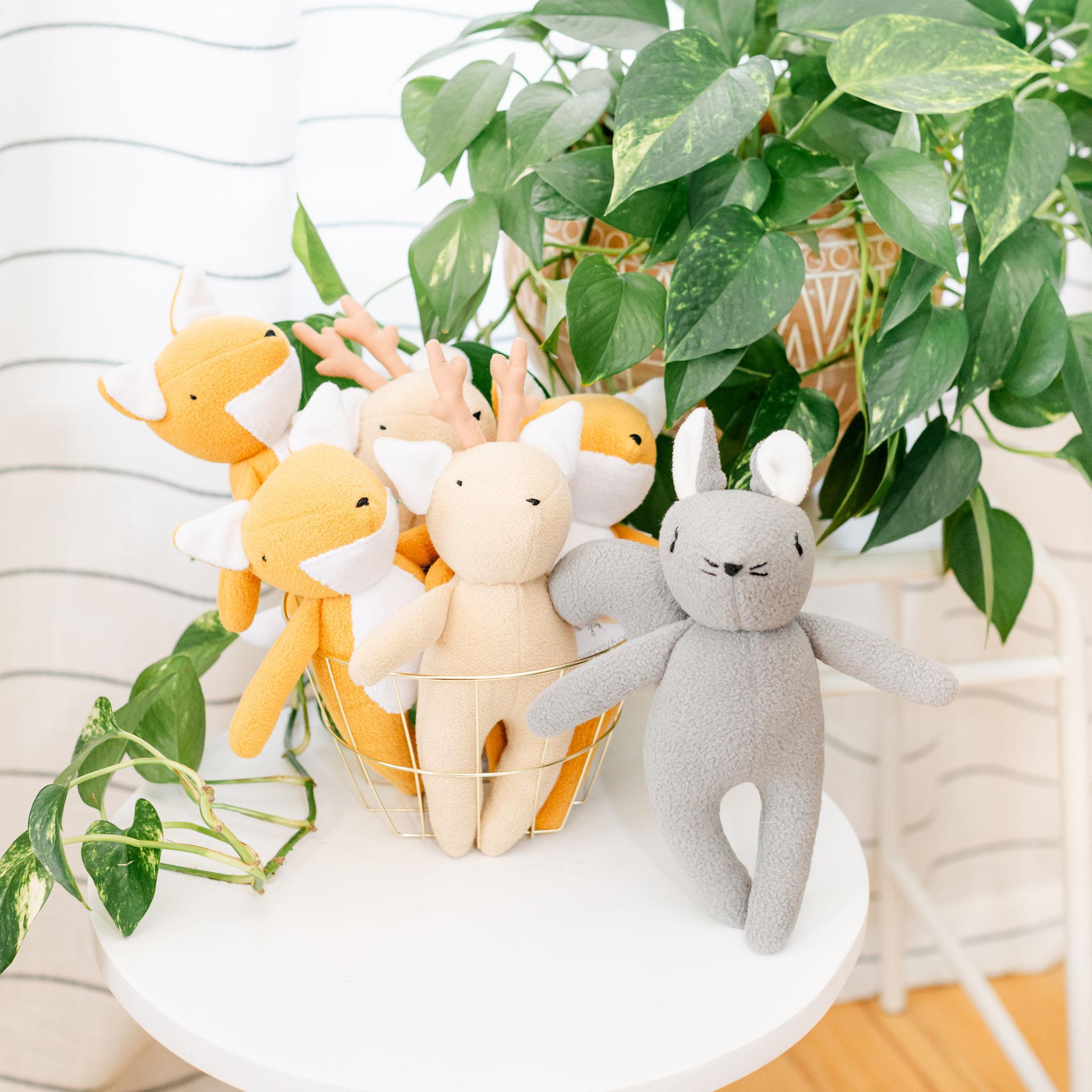 A display with plush animal toys in a gold basket on a white table with a plant in the background