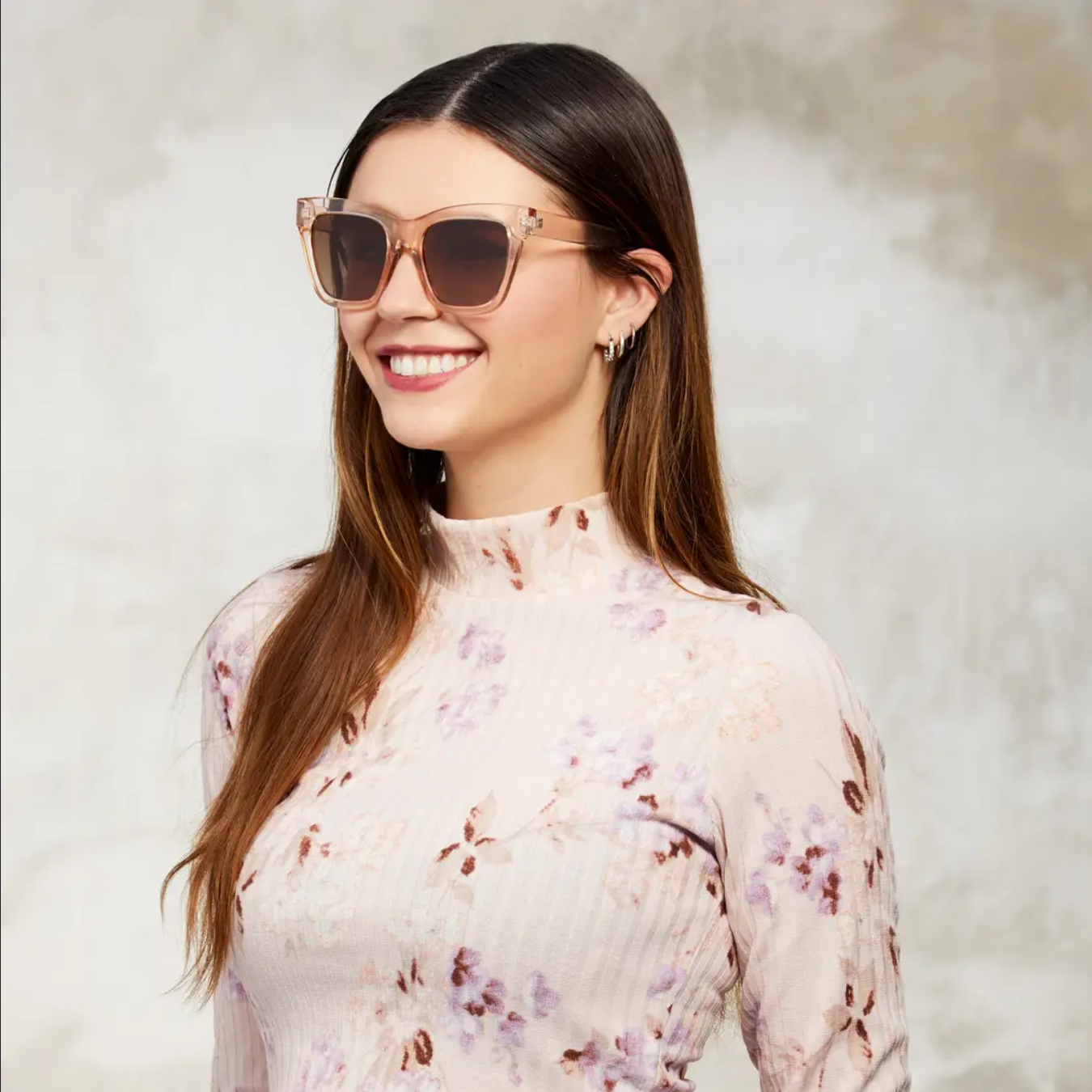 Woman wearing sunglasses and a floral top against a neutral background