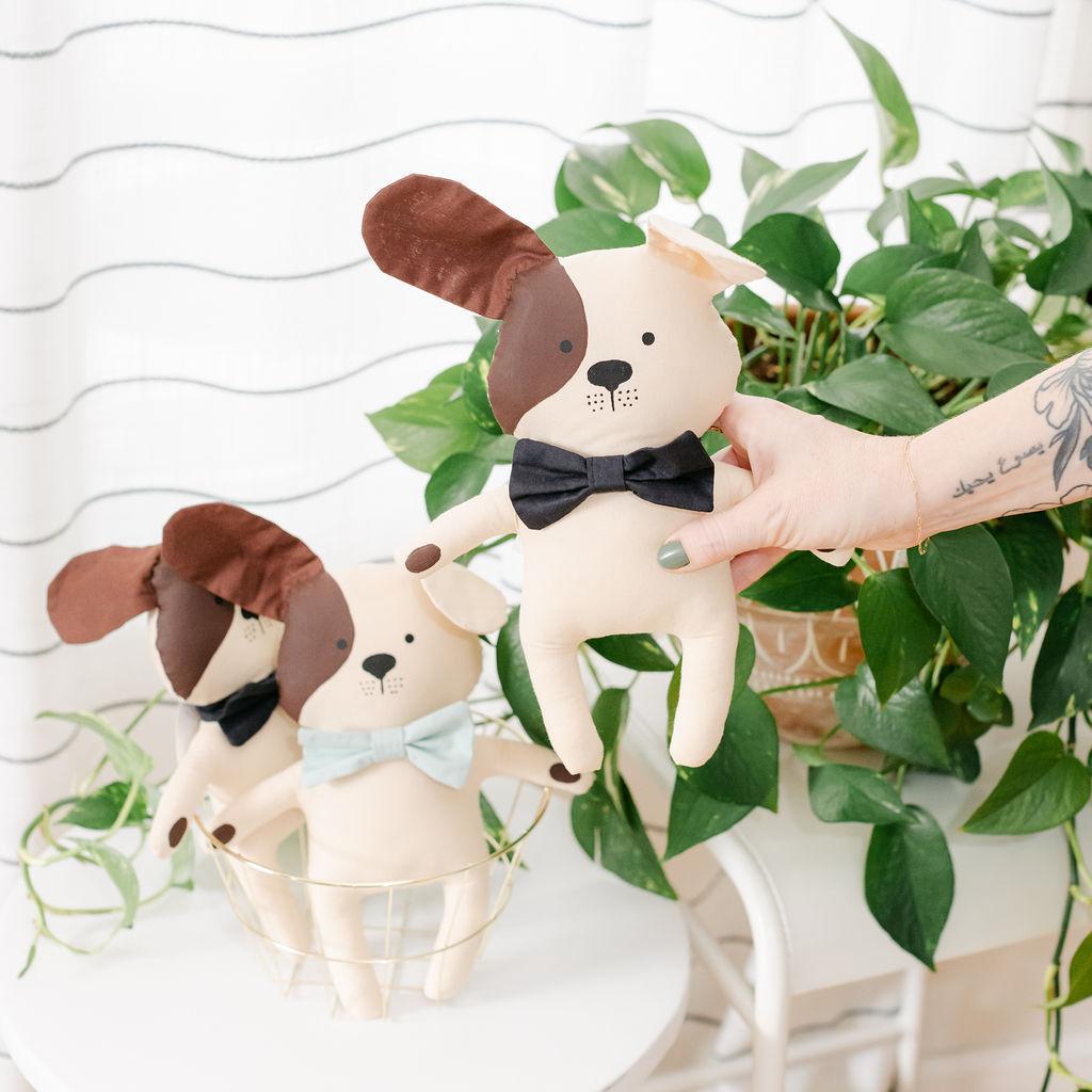 A person holding a stuffed dog toy with a plant in the background