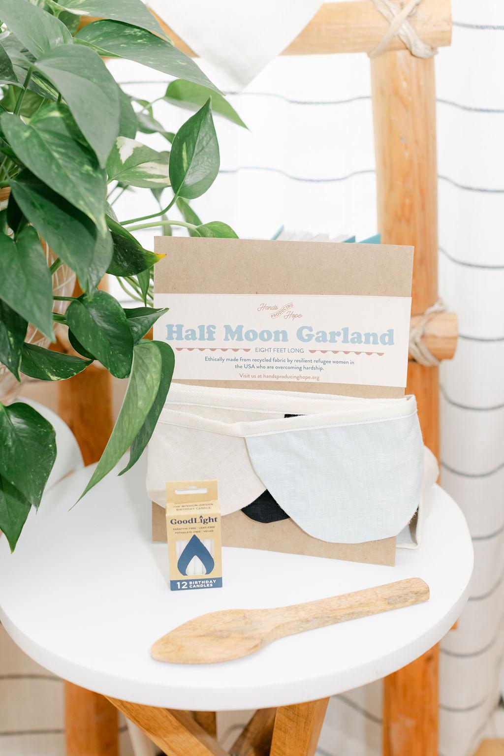 A display of party items including garland, candles and a wooden cake server on a white table with a plant in the background
