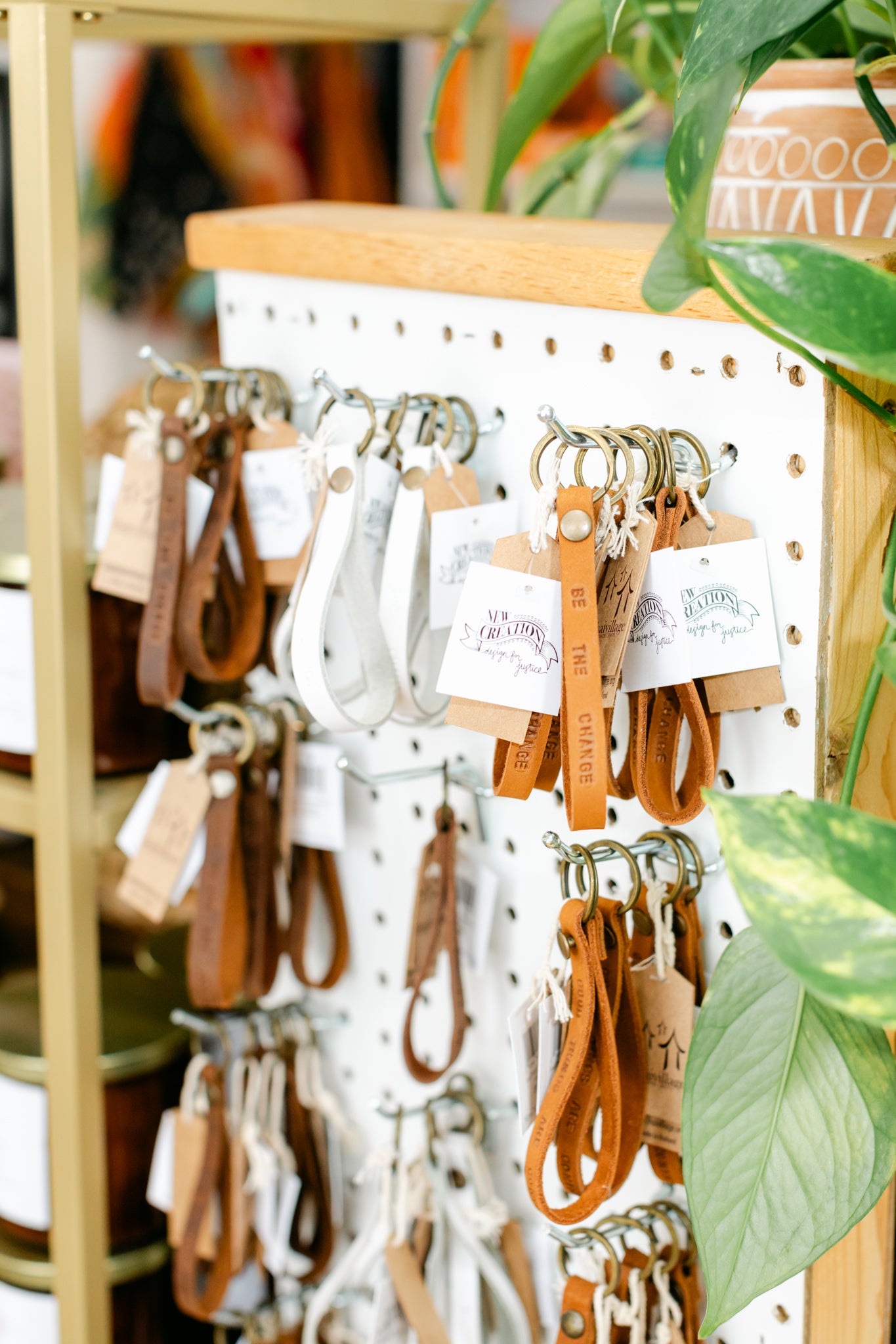 A display of leather loop keychains with stamped text with a plant in the foreground