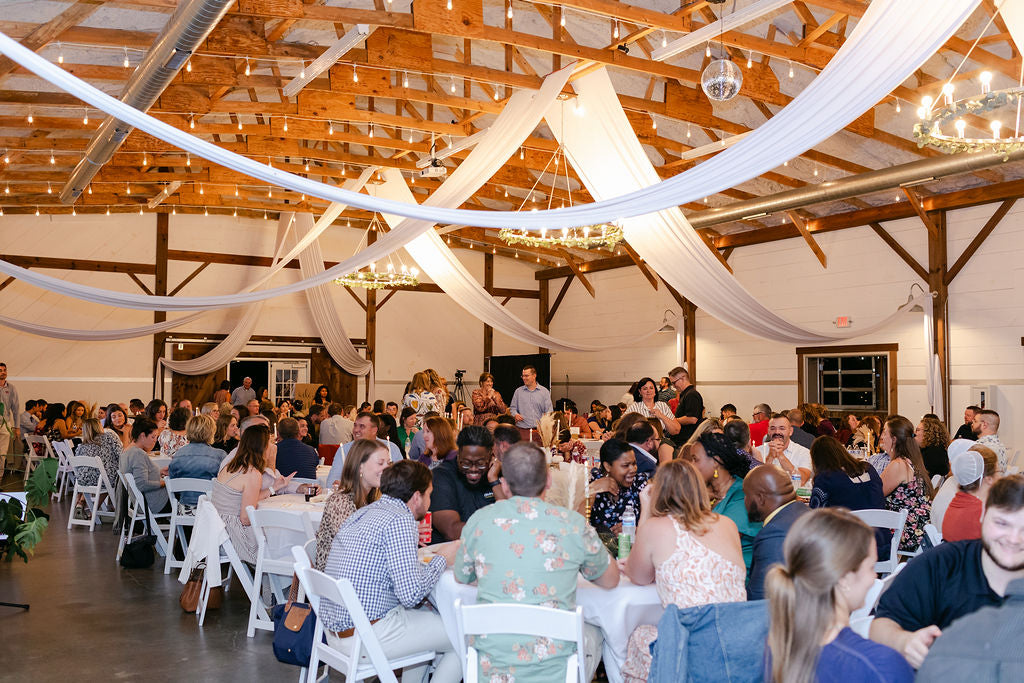 People gathered in a large hall with wooden beams and white fabric draped from the beams.