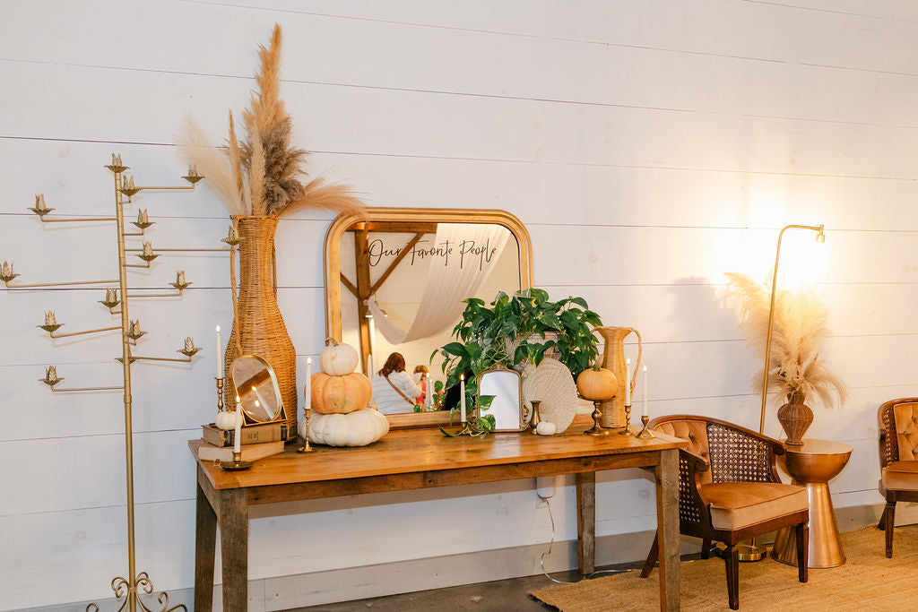 Decorative room setup with a wooden table, mirror, and plants against a white wall.