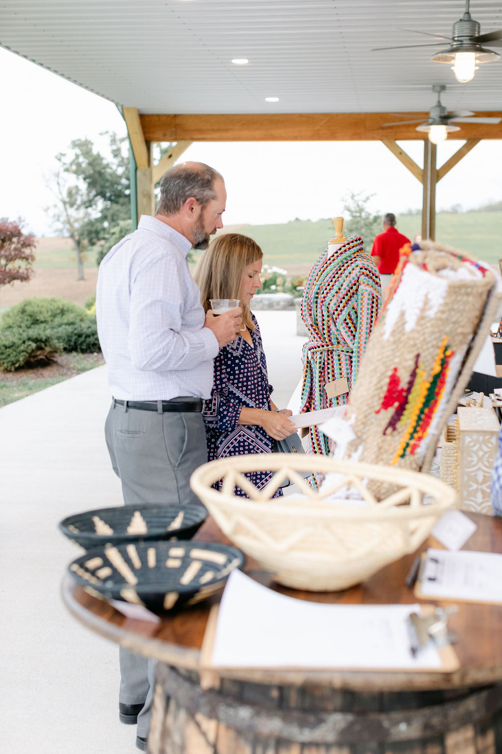 Two people standing near a table with decorative items outdoors under a covered area.