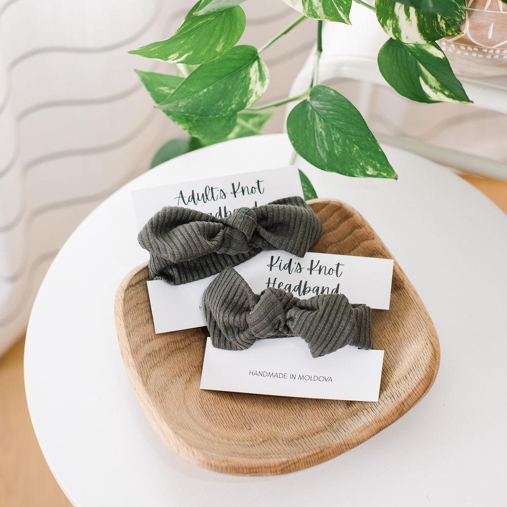 Two olive green knit headbands on a wooden tray with a card that reads &