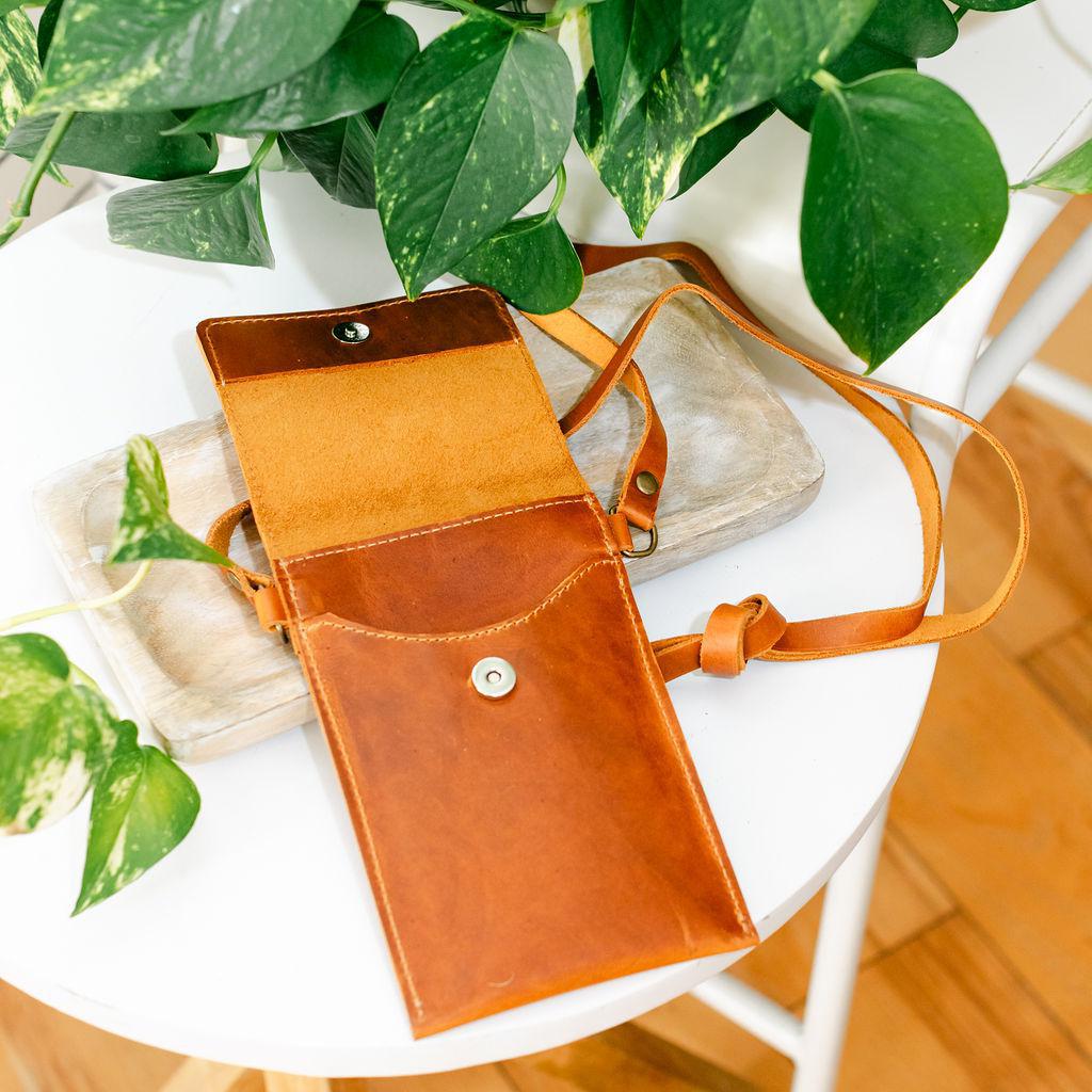 A small leather bag on a wooden display with a plant in the background