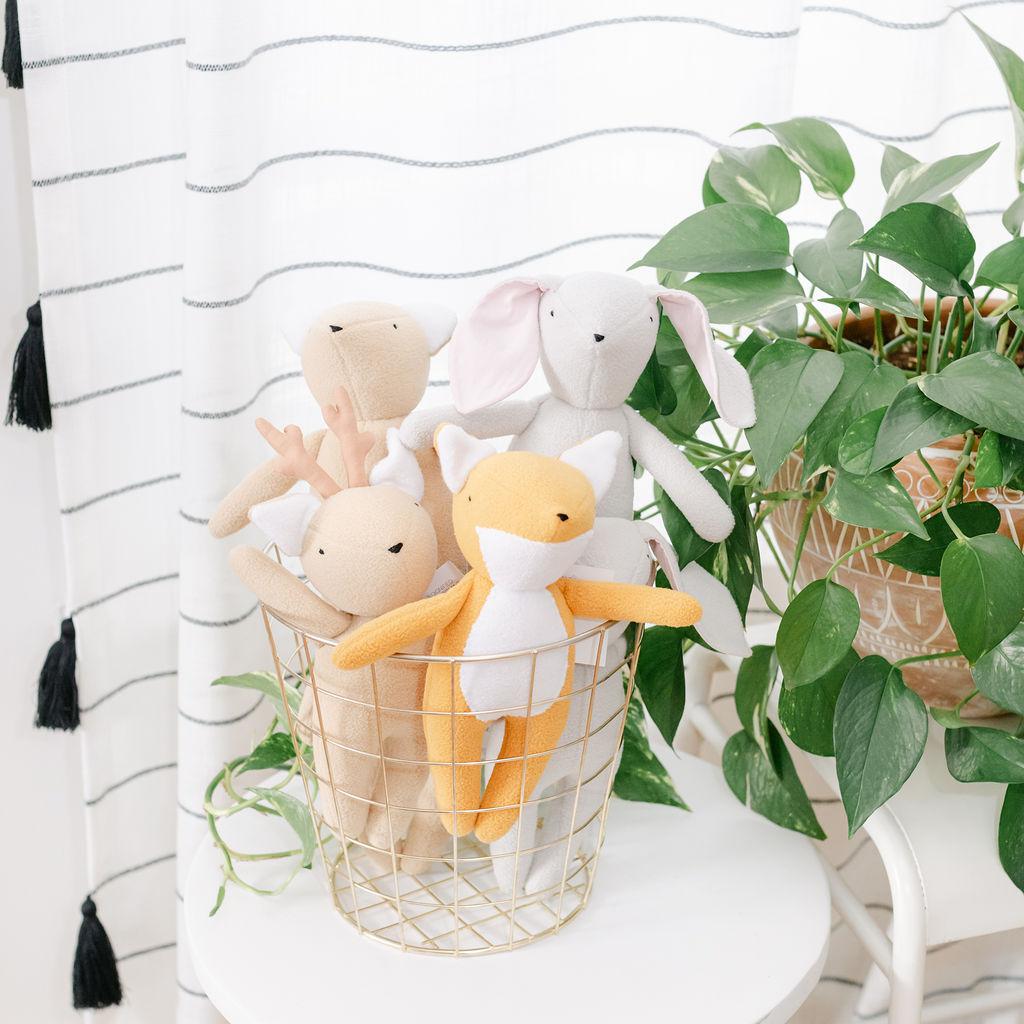 A set of plush animal toys in a brass basket on a white table with a plant in the background