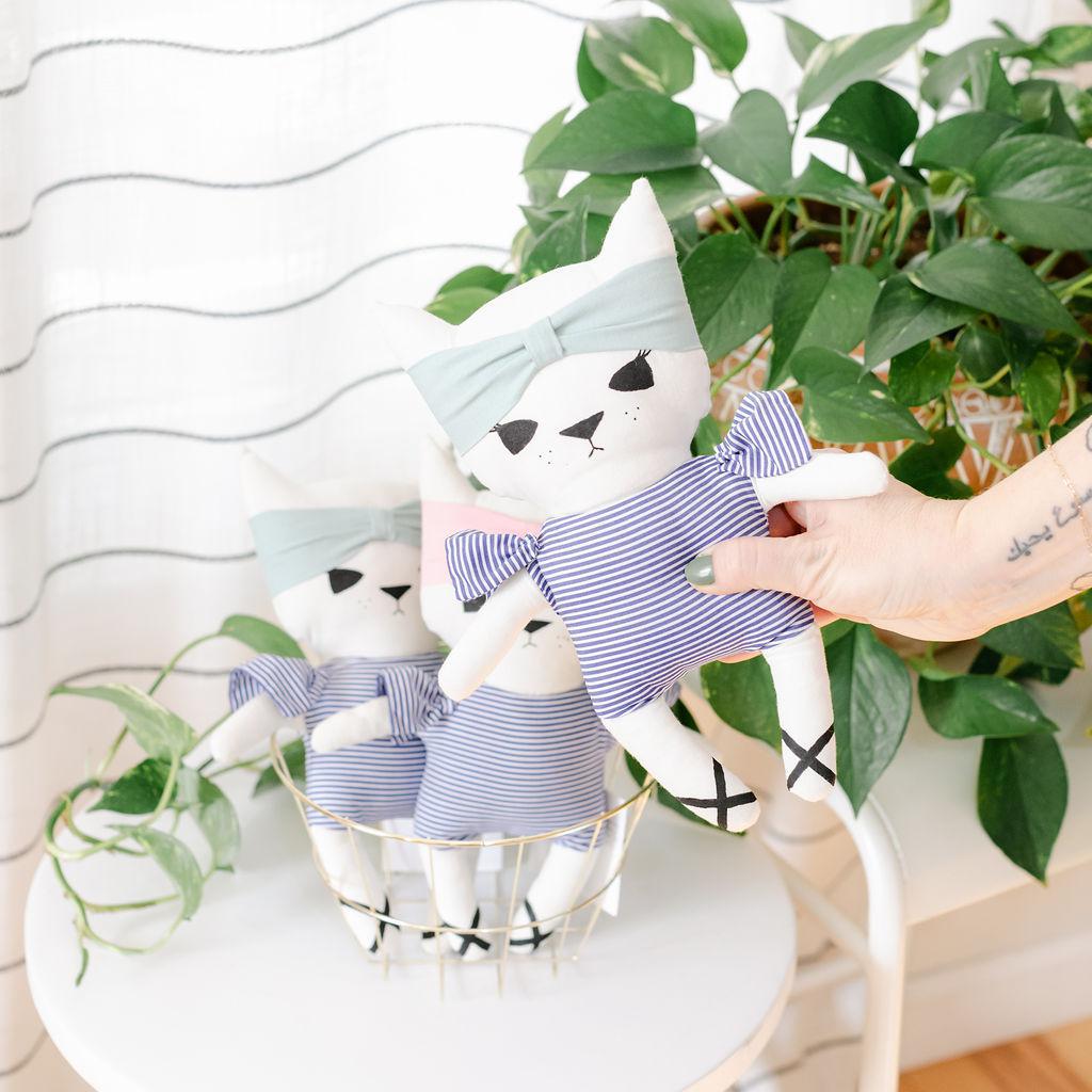 A person holding a stuffed cat toy with blue stripes and a headband with a plant in the background