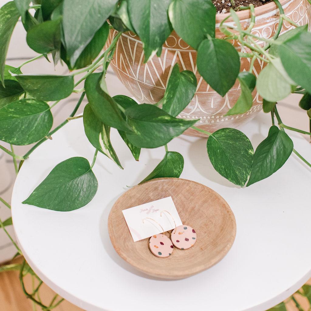 Wooden dish with earrings and a card on a white surface with green leaves in the background