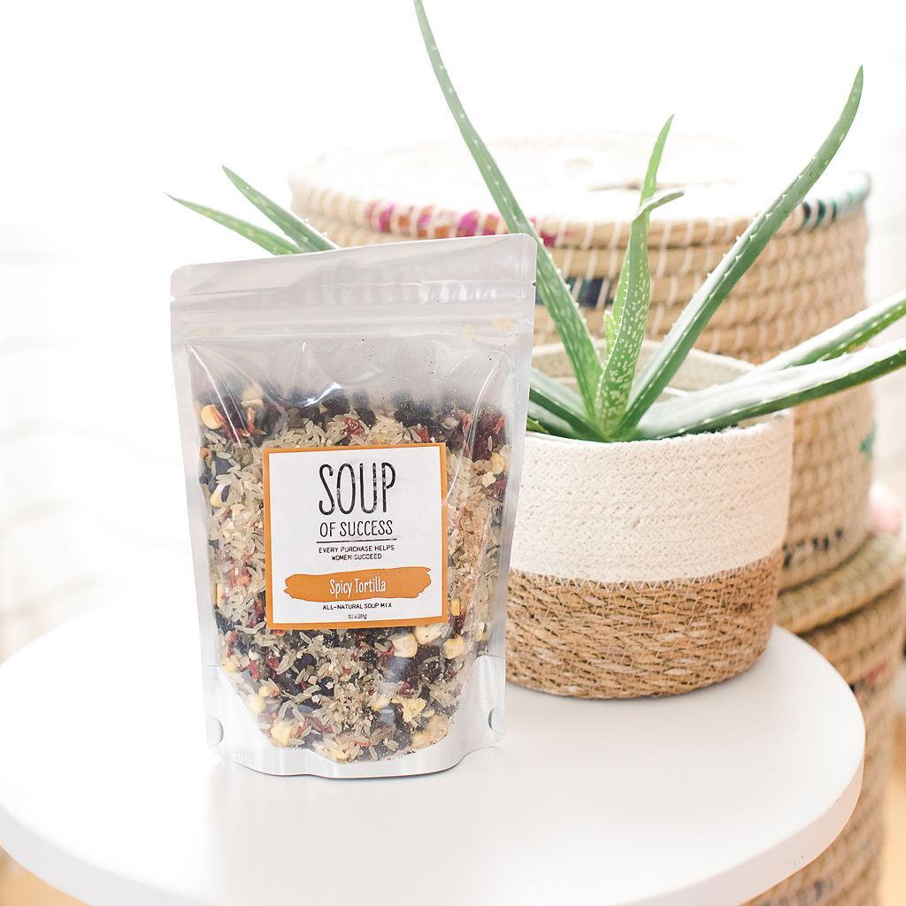 Packaged Spicy Tortilla Soup mix from Soup of Success, placed on a white surface with a potted plant in the background.
