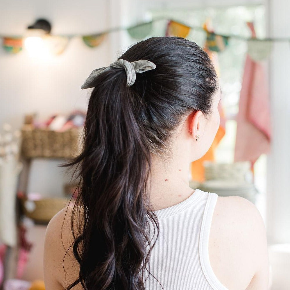 Young woman shot from behind with dark hair in a pony tail wearing a light gray fabric hair tie.