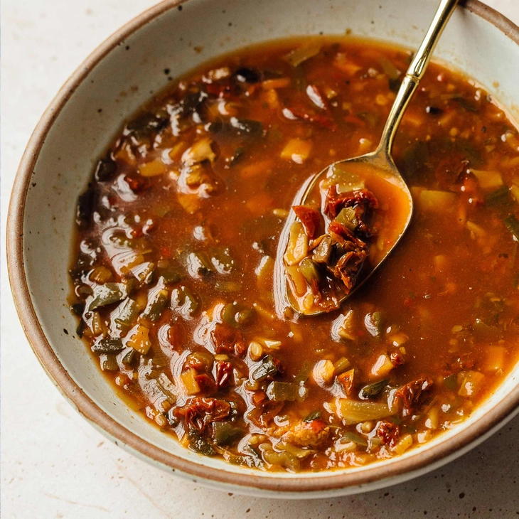 A bowl of vegetable soup with a spoon on a white surface.