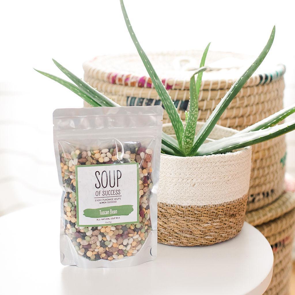 A package of Tuscan Bean Soup mix from Soup of Success on a white table with a plant in the background.