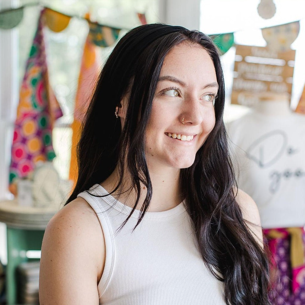 Smiling young woman looking away from the camera wearing a black headband in her hair with a colorful blurred background.