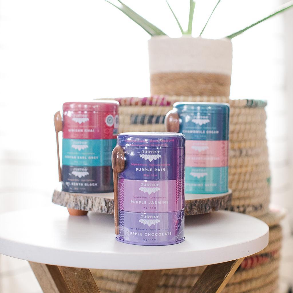 Three cylindrical tins with labels, arranged on a table, each with a unique color theme corresponding to the tea flavors inside.
