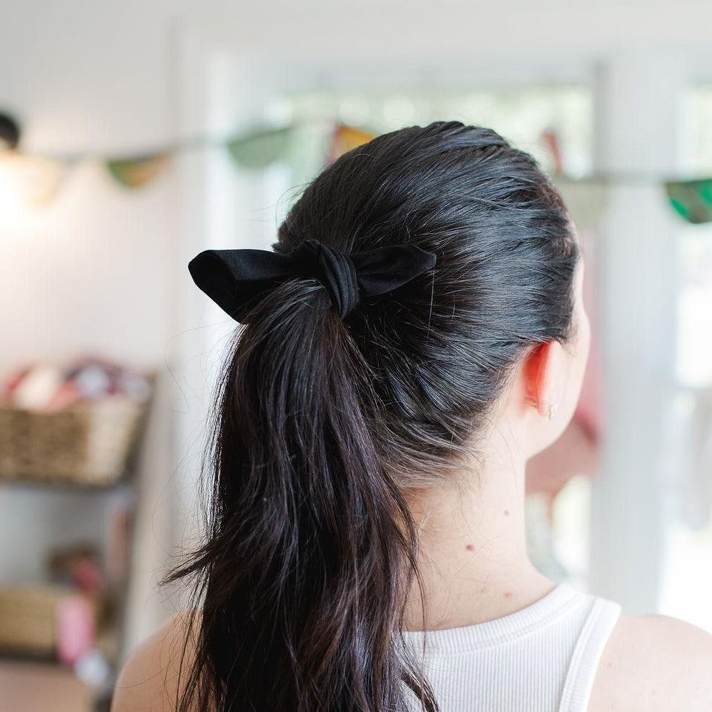 Young woman shot from behind with dark hair in a pony tail wearing a black fabric hair tie.