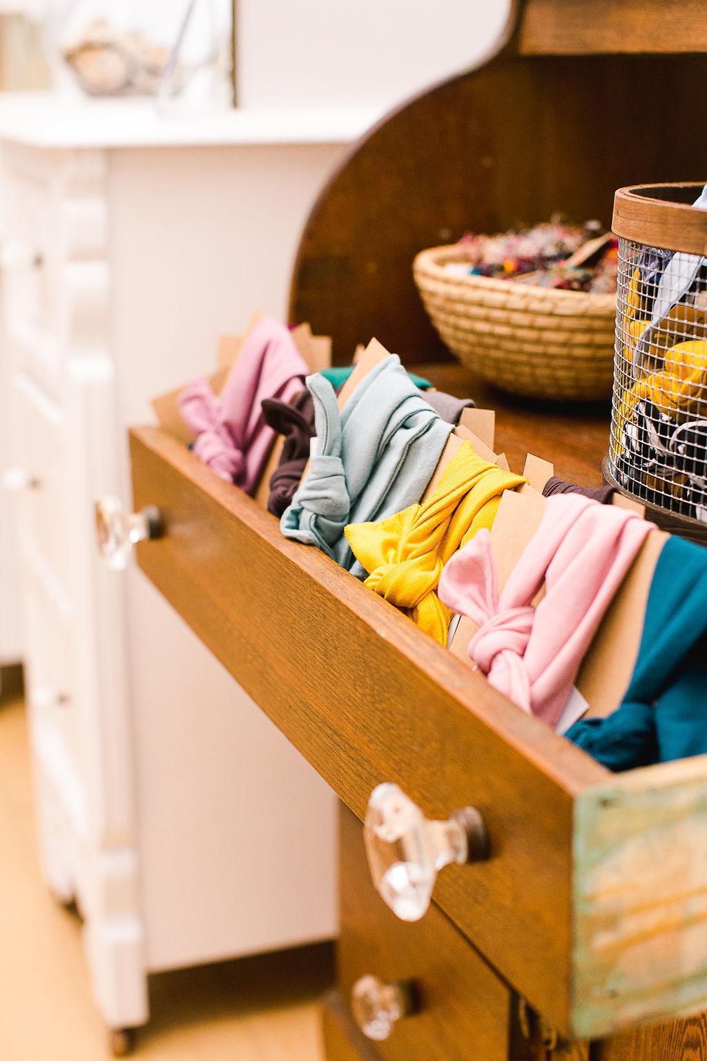 Open drawer of a wooden piece of furniture. Inside the drawer is a colorful selection of headbands on cards.