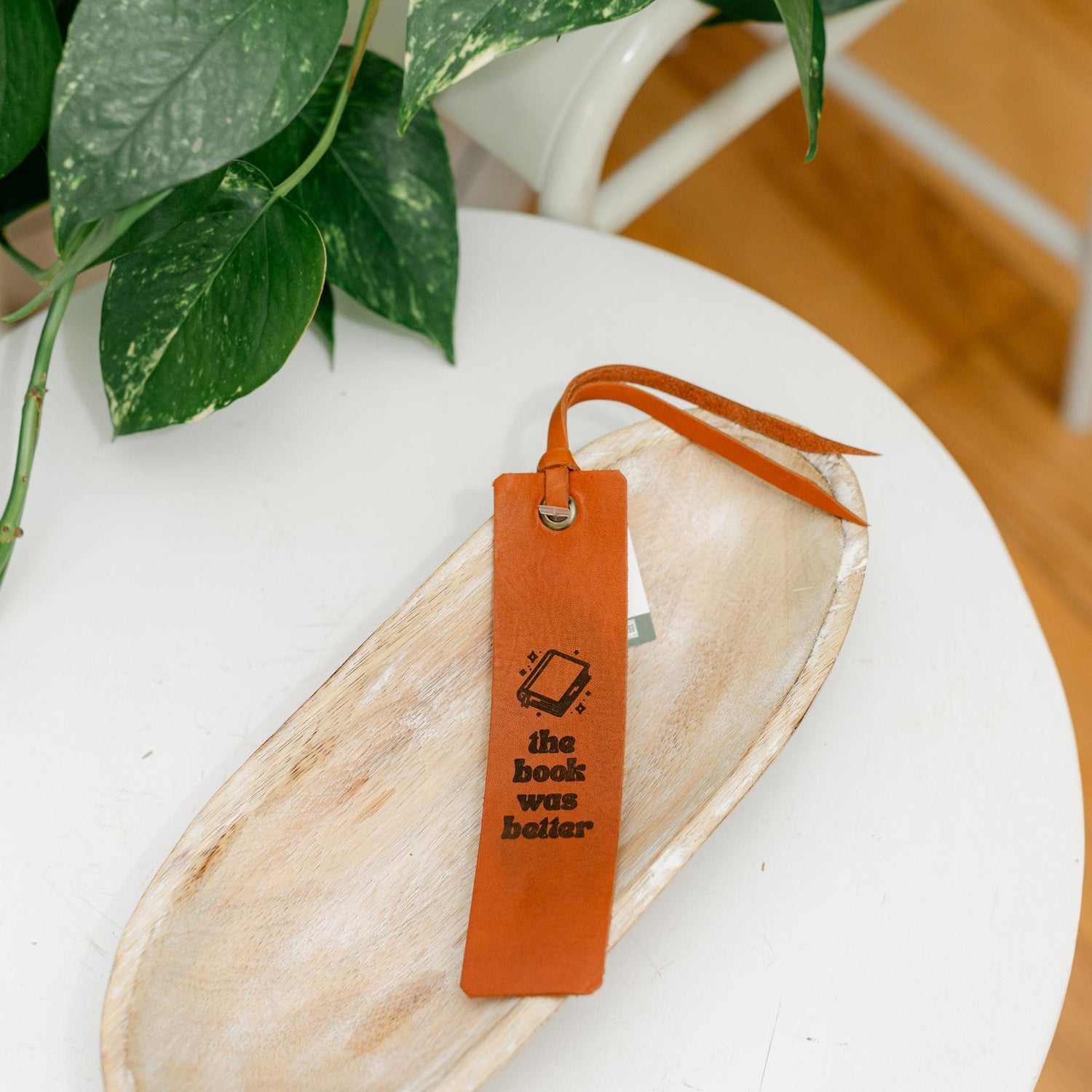Leather bookmark with text on a white surface with a plant in the background