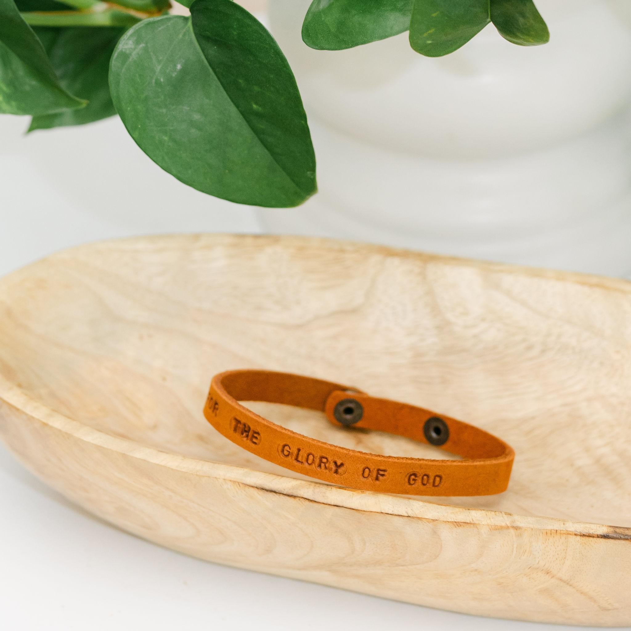 Light brown leather bracelet with For the Glory of God engraved sitting in a wooden dish
