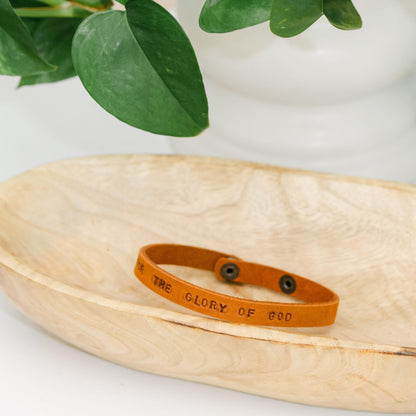 Light brown leather bracelet with For the Glory of God engraved sitting in a wooden dish