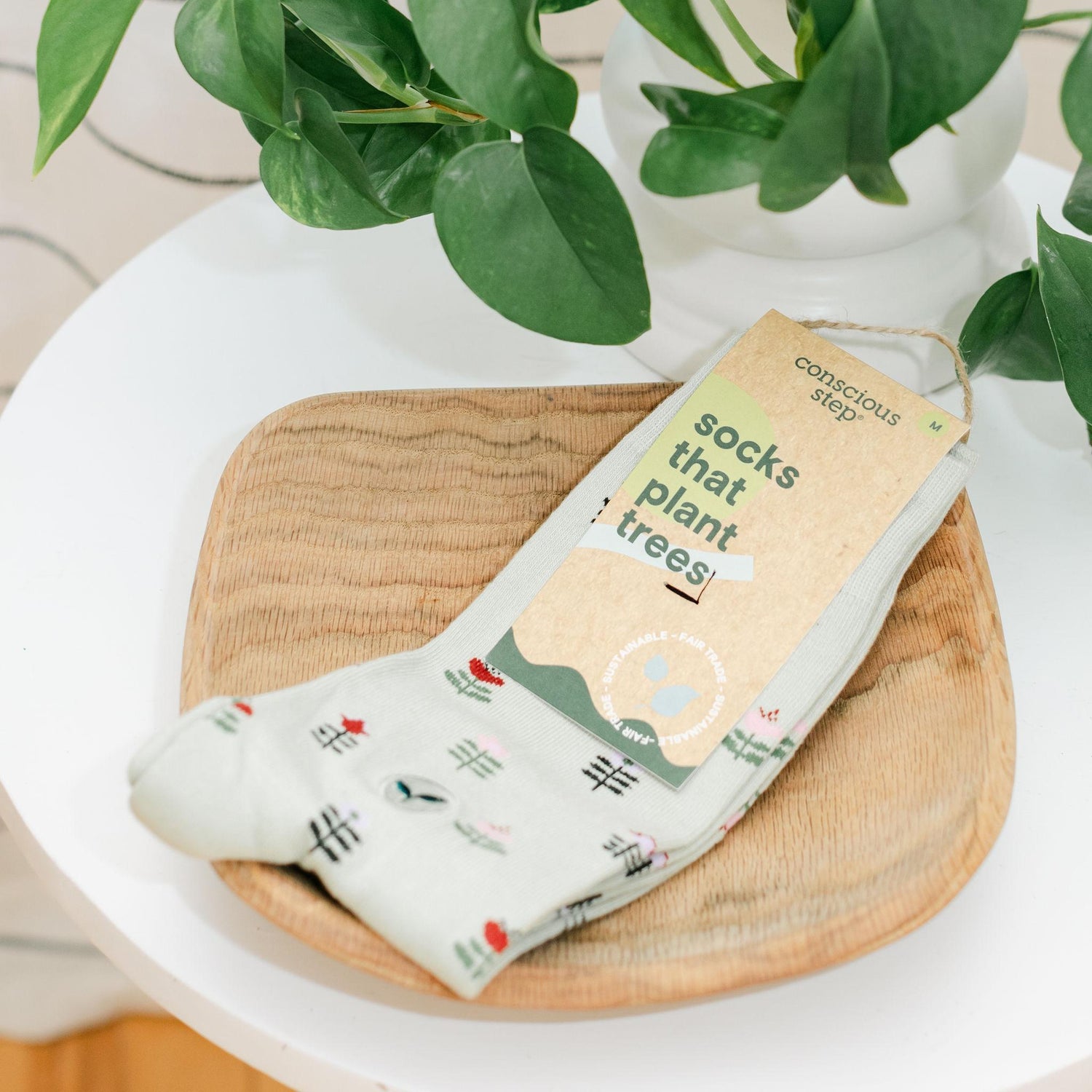 Light green socks with flowering plant design in a wooden tray with a plant in the background