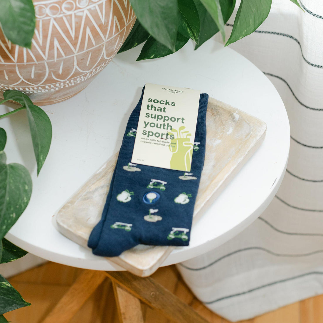 A pair of navy blue crew socks with a green and white graphic print and a paper tag reading &