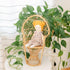 A doll with white skin and red hair buns, dressed in a floral outfit, sitting in a wicker basket.