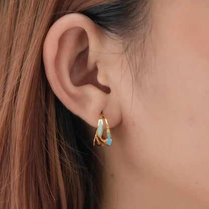 Close-up of an ear wearing a gold earring with turquoise stone