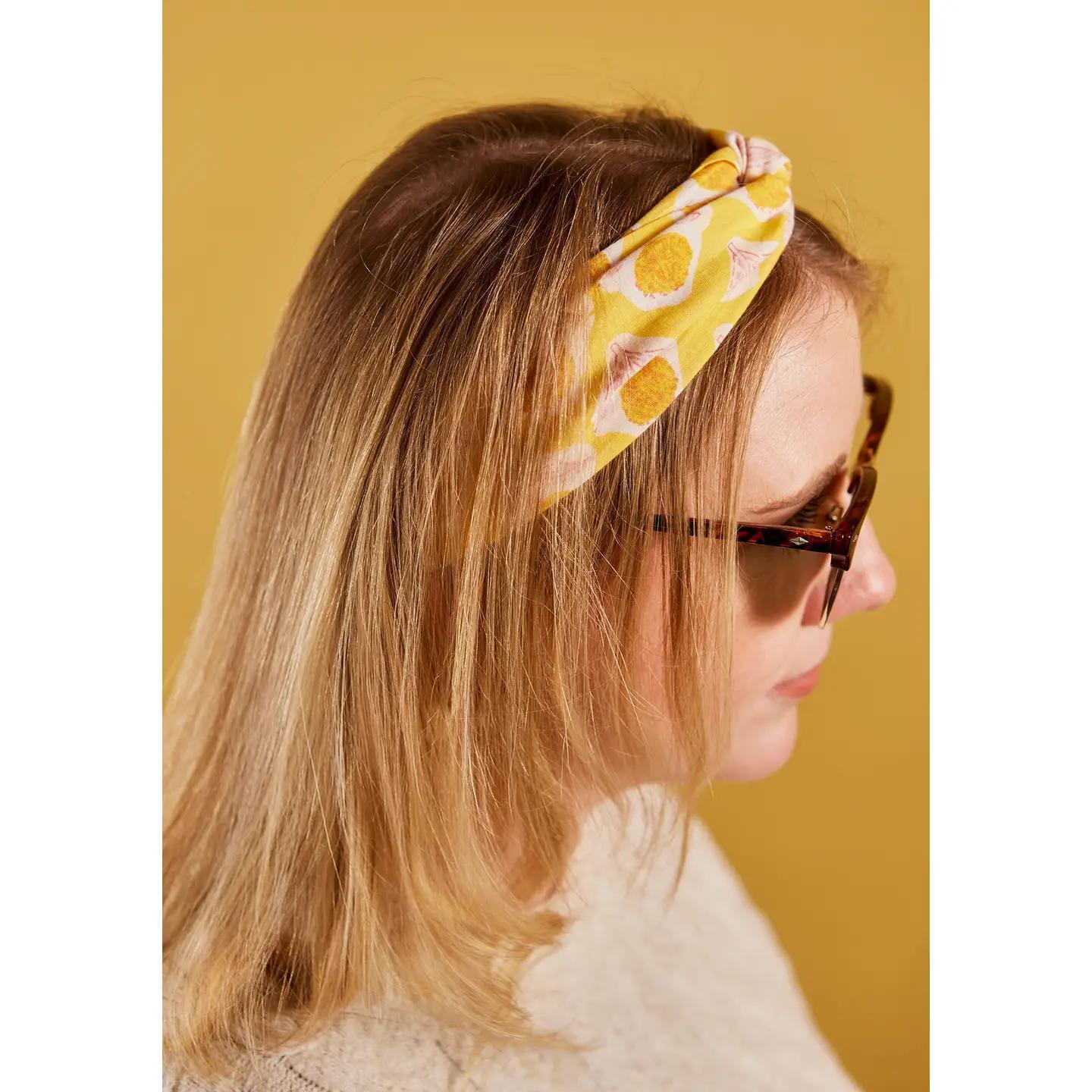 Woman wearing a yellow floral headband against a mustard yellow background