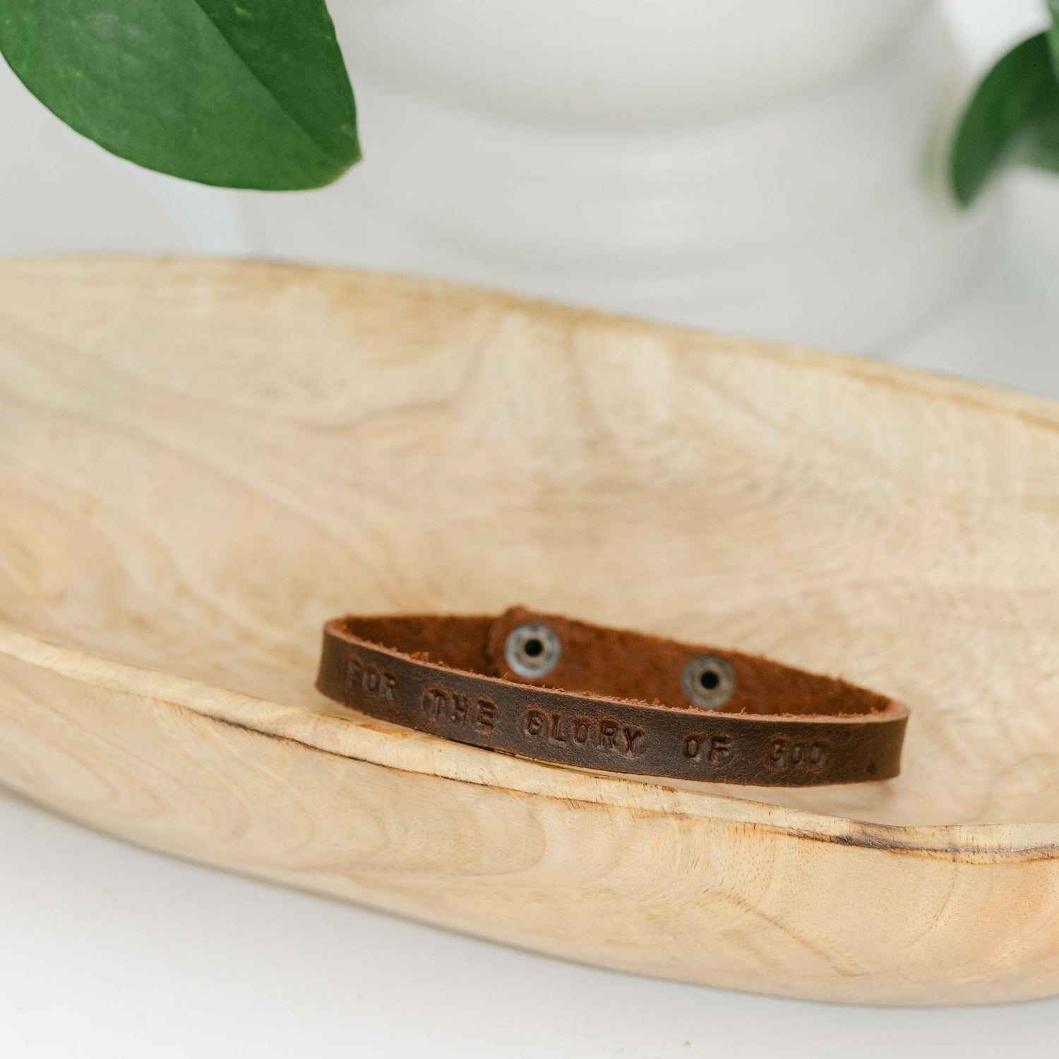 Dark brown leather bracelet with For the Glory of God engraved sitting in a wooden dish