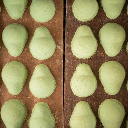 Green bath bombs shaped like avocados on a wooden table.