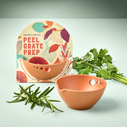 Small terracotta bowl with a spout and holes in the foreground. In the background is a second bowl in colorful packaging featuring the words "Peel, Grate, Prep" and herbs.