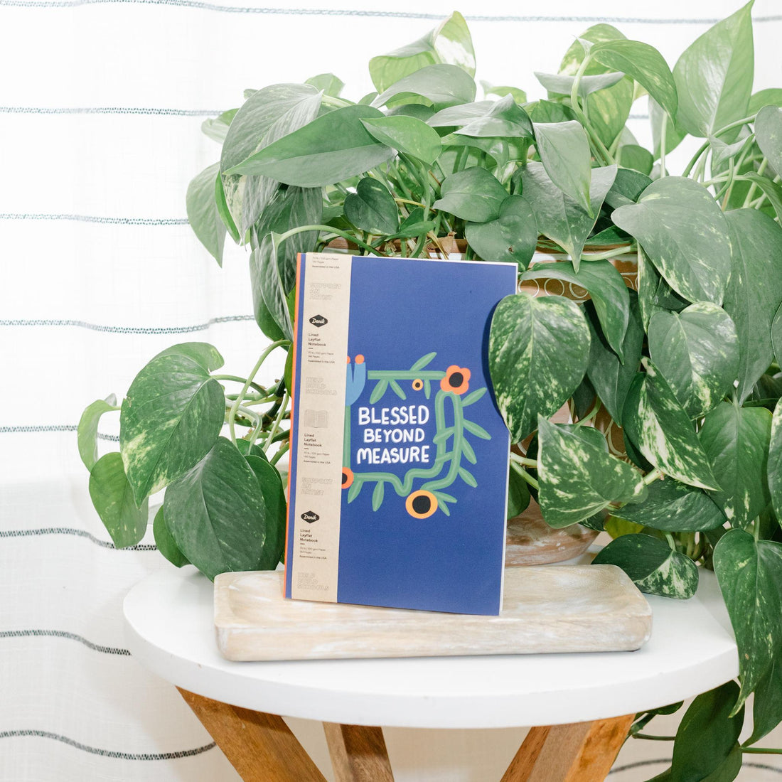 Blue notebook with text and floral illustrations on a wooden stand with plants in the background