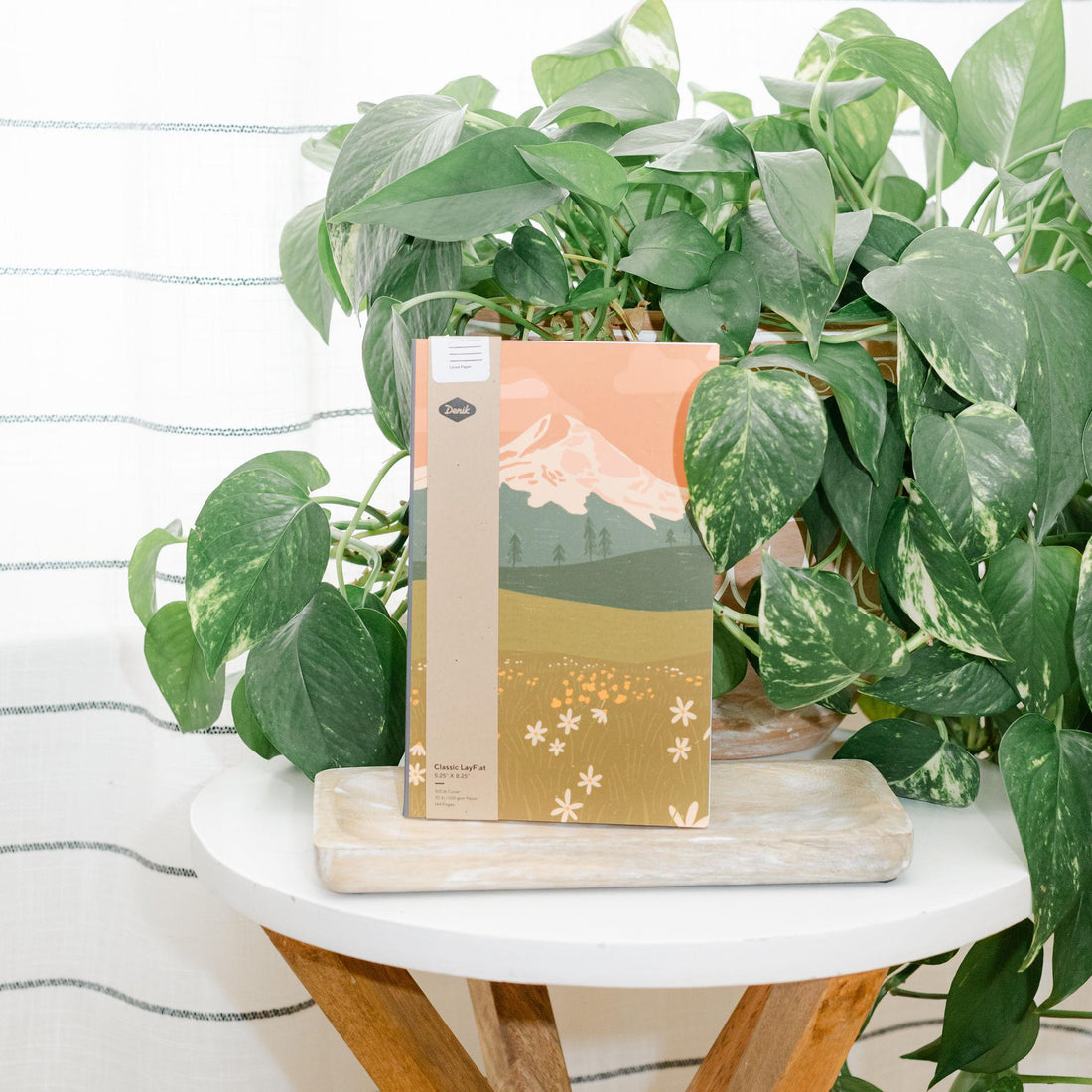 Notebook with mountain design on a small table surrounded by green plants