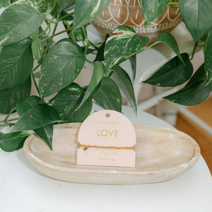 Gold bead bracelet on a card labeled &