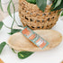 A colorful bookmark with text, placed on a wooden surface with a woven basket and green leaves in the background.