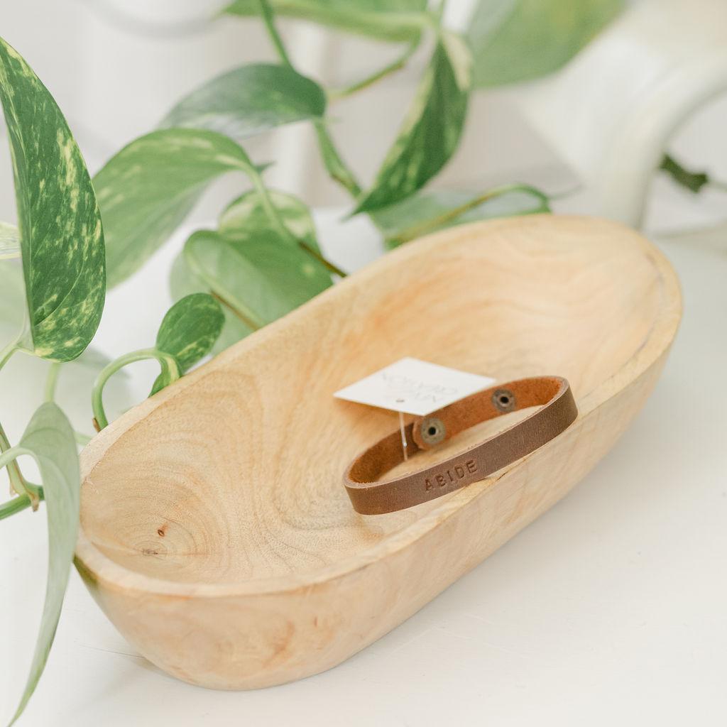 Wooden dish with a brown leather bracelet with the word &